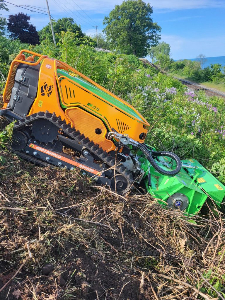 Remote-controlled Green Climber mowing heavy brush on a steep embankment in Northwest Indiana